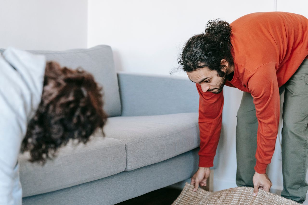 A couple straightening up their living room, arranging furniture and rugs together as a team.